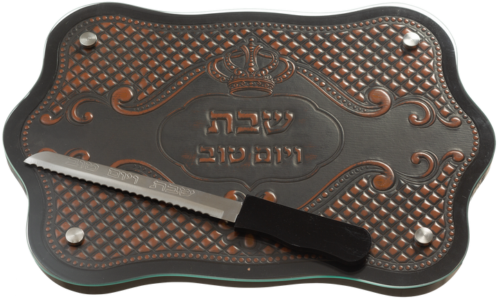 Scalloped glass challah board over brown and copper leather-look design with crown, knife resting on top