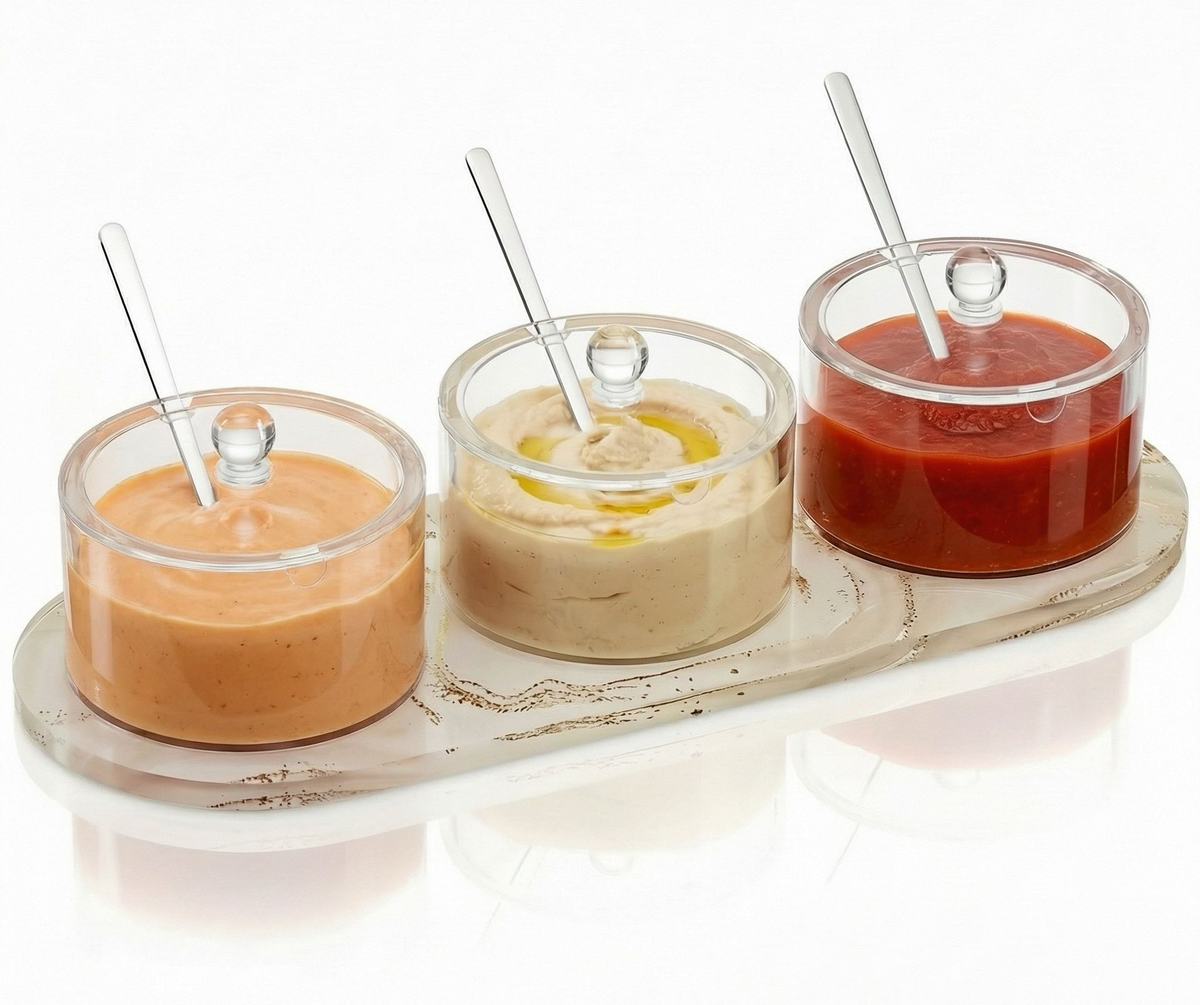 Clear three-bowl dip holder on a tray with lids and spoons, filled with three different dips