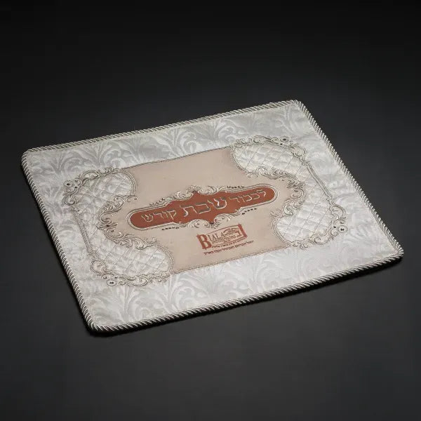 Silver-gray brocade challah cover with rose-colored center panel and Hebrew Shabbos lettering, flat on dark background