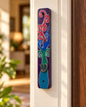 Tree of life mezuzah case in purple, red and teal mounted on a doorframe
