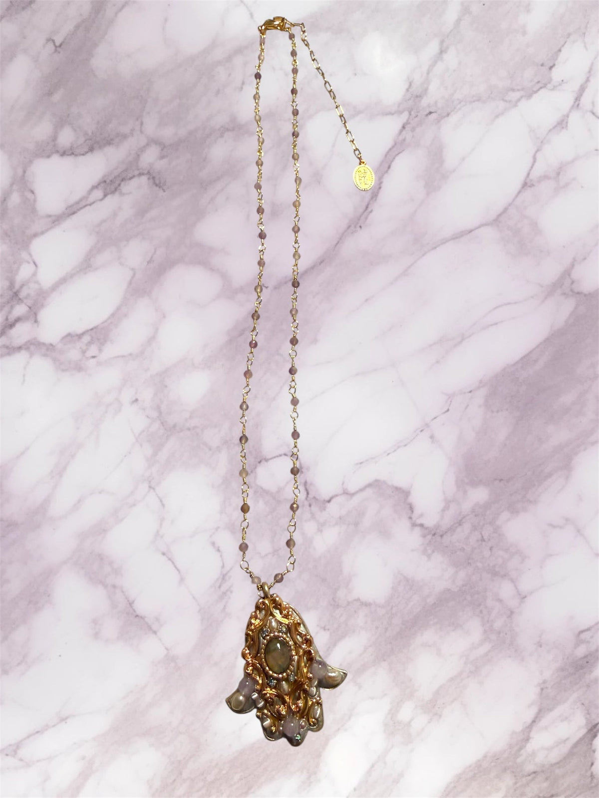 Michal Golan Abalone & Amethyst Hamsa Necklace, gold-plated hamsa necklace on a marble surface