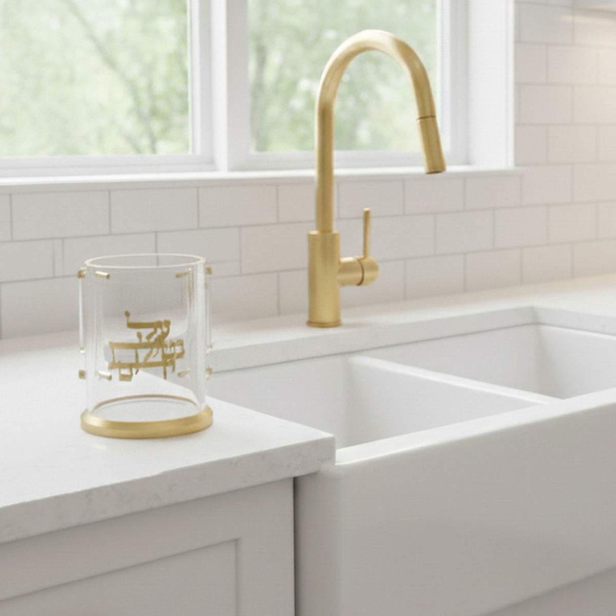 Gold monogram washing cup on a white kitchen counter beside a farmhouse sink and brass faucet