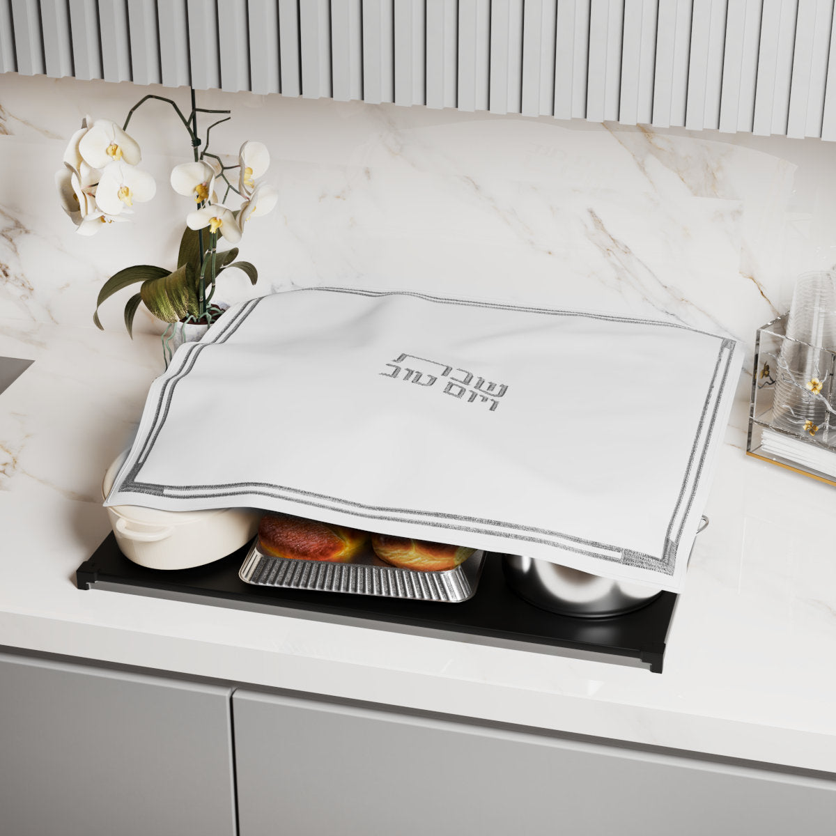 Cover draped over pans on a hot plate on a marble kitchen counter