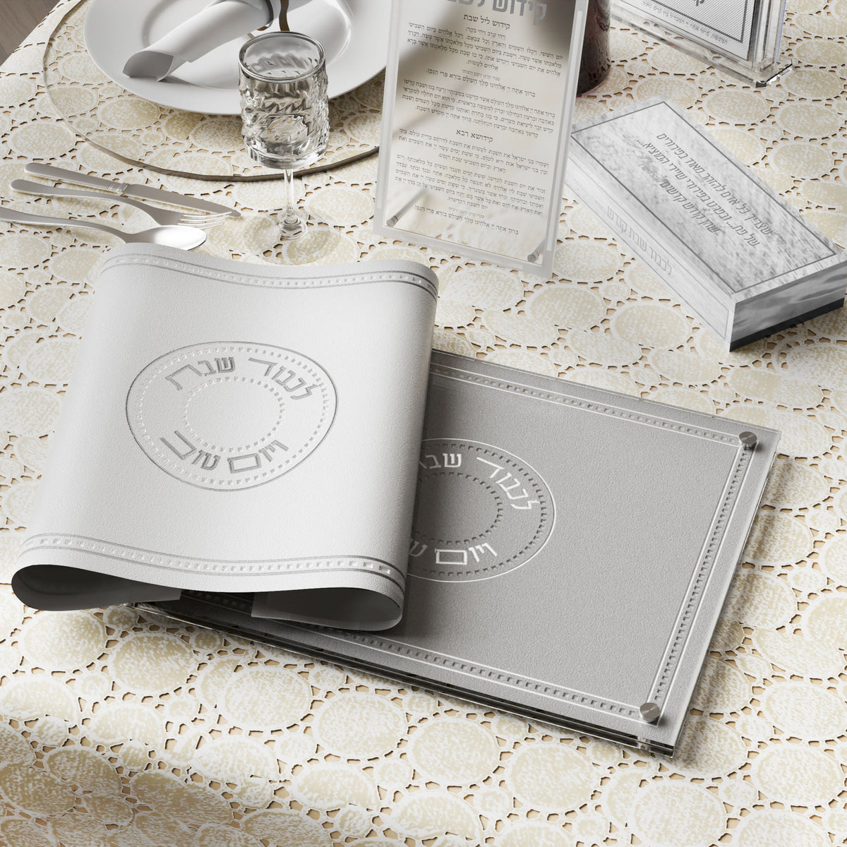 White and silver challah cover rolled over a gray challah board on a set Shabbos table