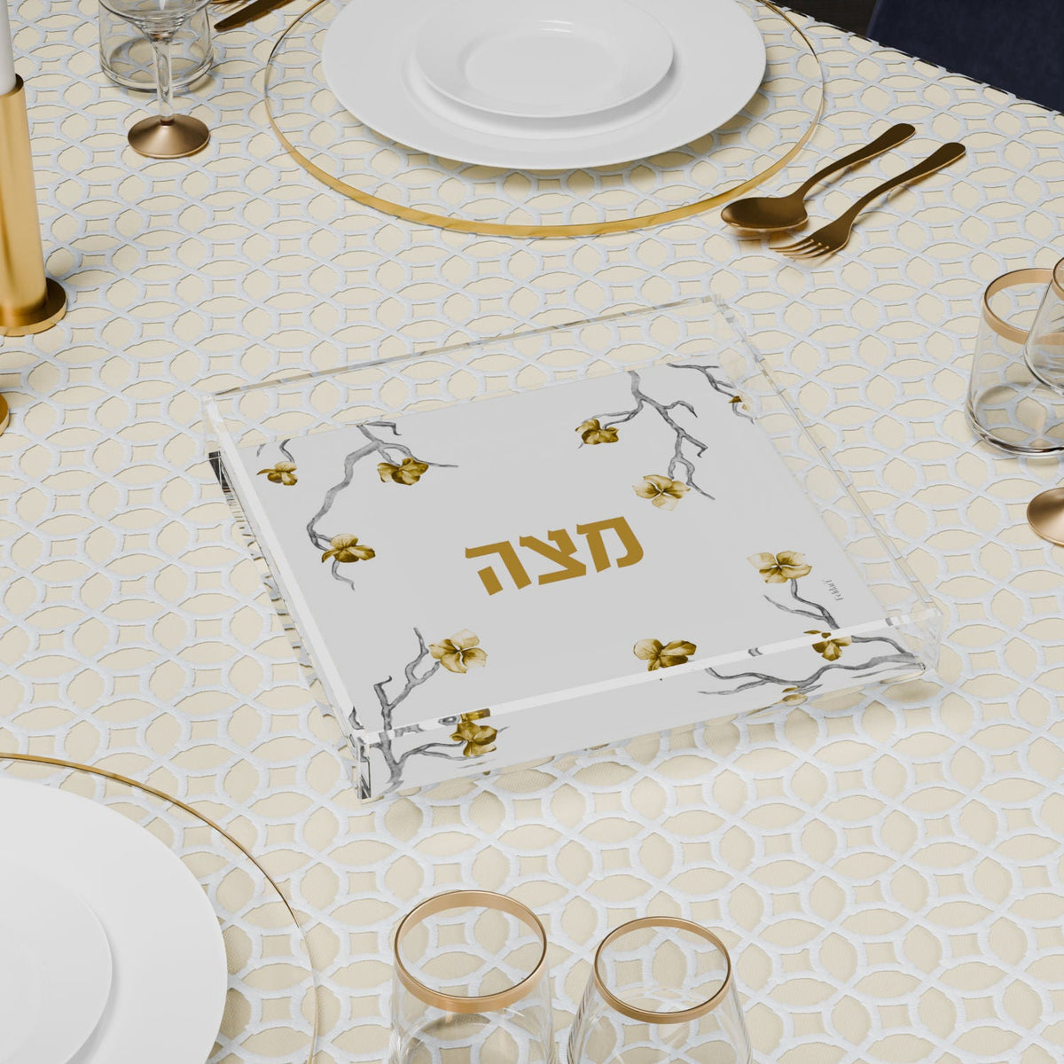 Square matzah plate on a set seder table between gold-rimmed plates and glasses