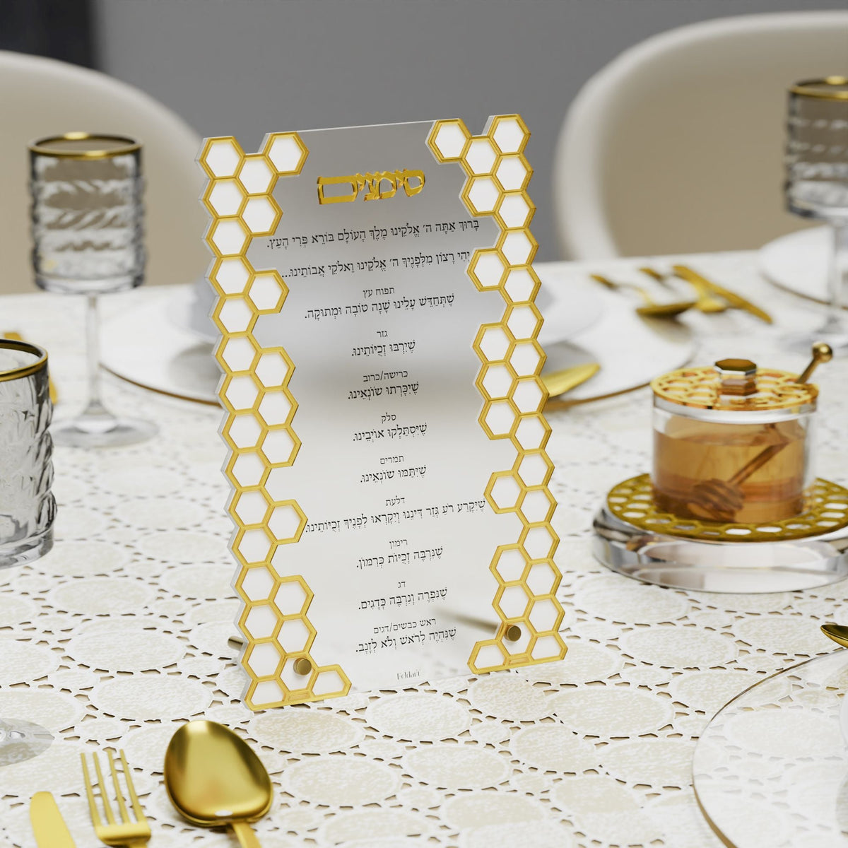 Gold honeycomb simanim card on a lace-covered table beside a gold honey dish