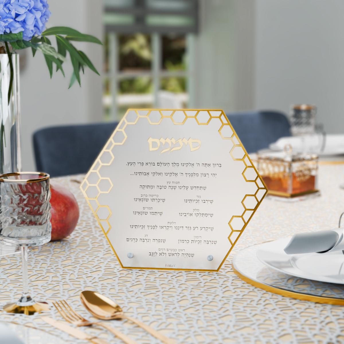 Gold simanim card standing on a Rosh Hashanah table beside a honey dish and pomegranate