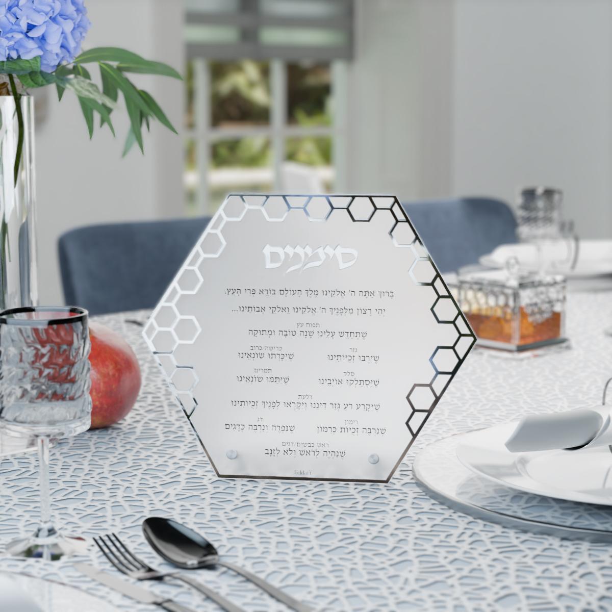 Silver simanim card on a set table with a silver honey dish and wine glass