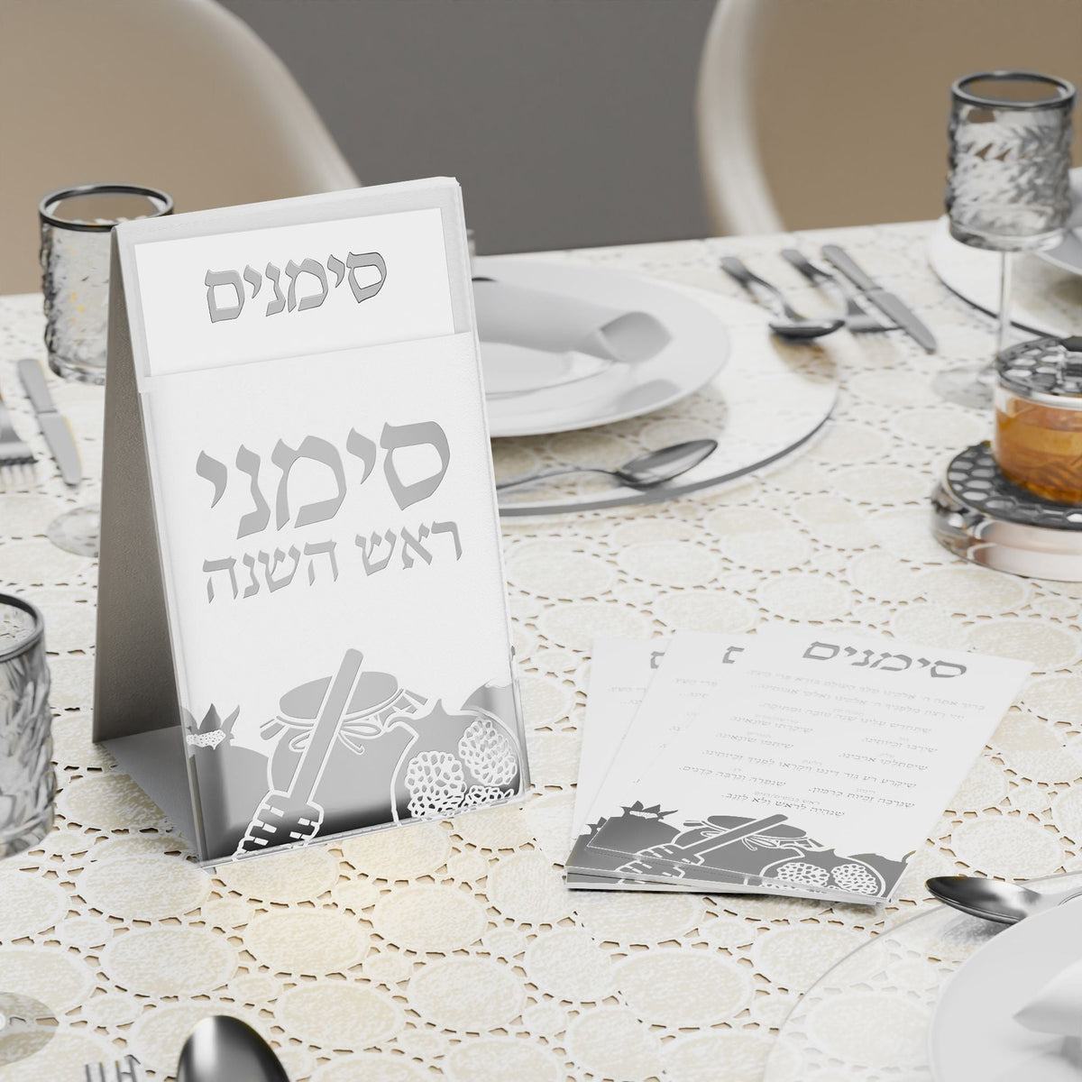 Silver simanim pouch and cards set on a white table with glassware and silver cutlery