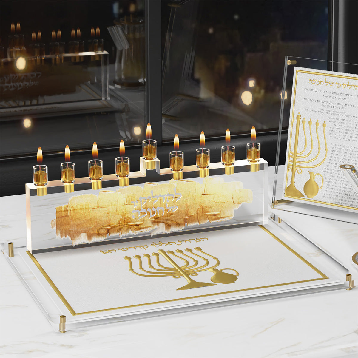Brochos card beside a lit lucite menorah on a matching gold tray by a night window