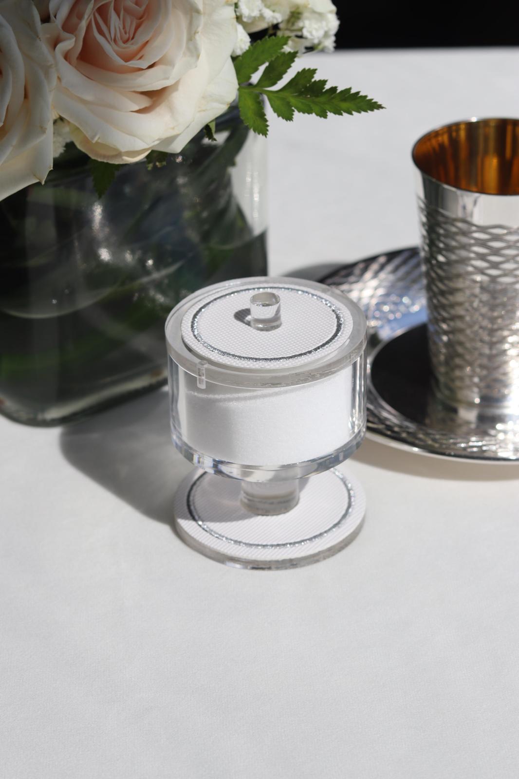 Salt holder with silver trim on a white tablecloth beside a silver kiddush cup and roses