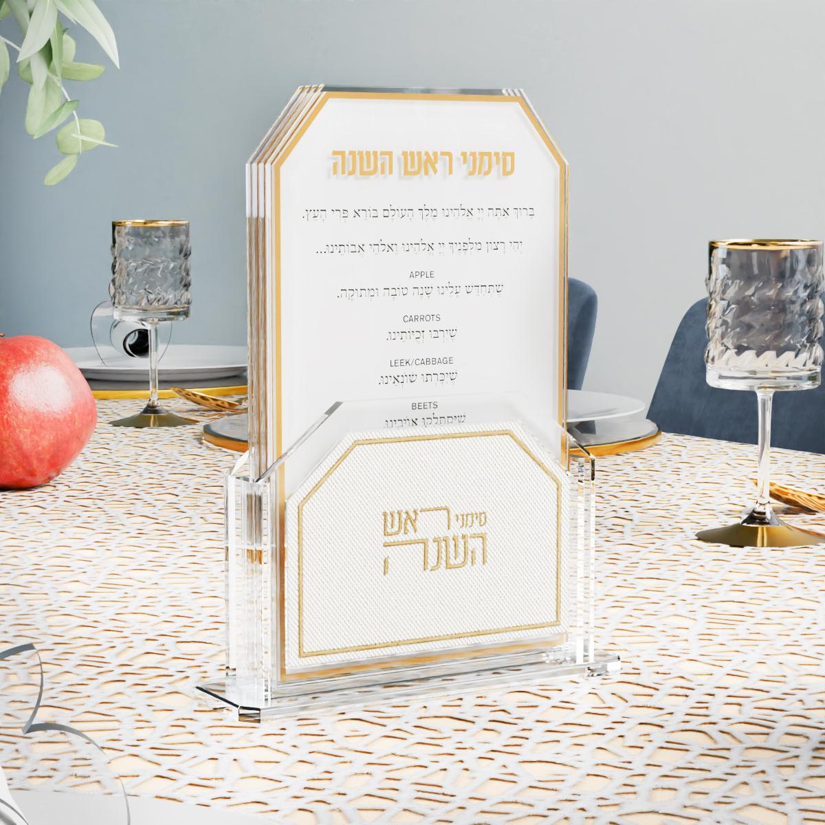 Gold simanim cards on a Yom Tov table with a pomegranate and crystal cups