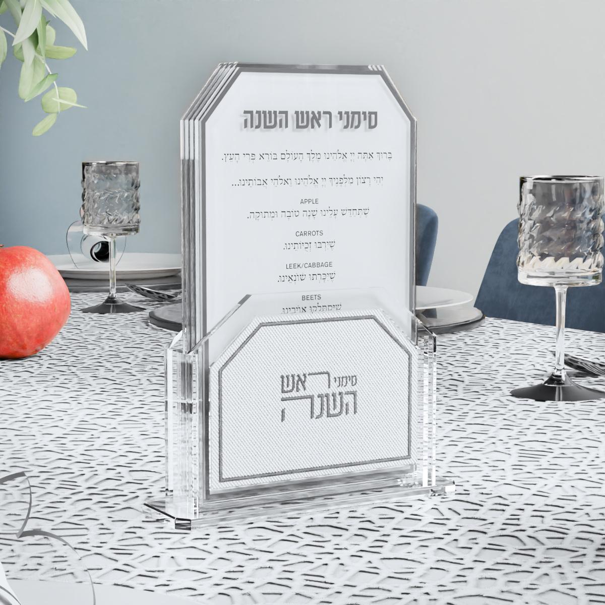 Silver simanim holder on a silver lace tablecloth beside a pomegranate and goblets