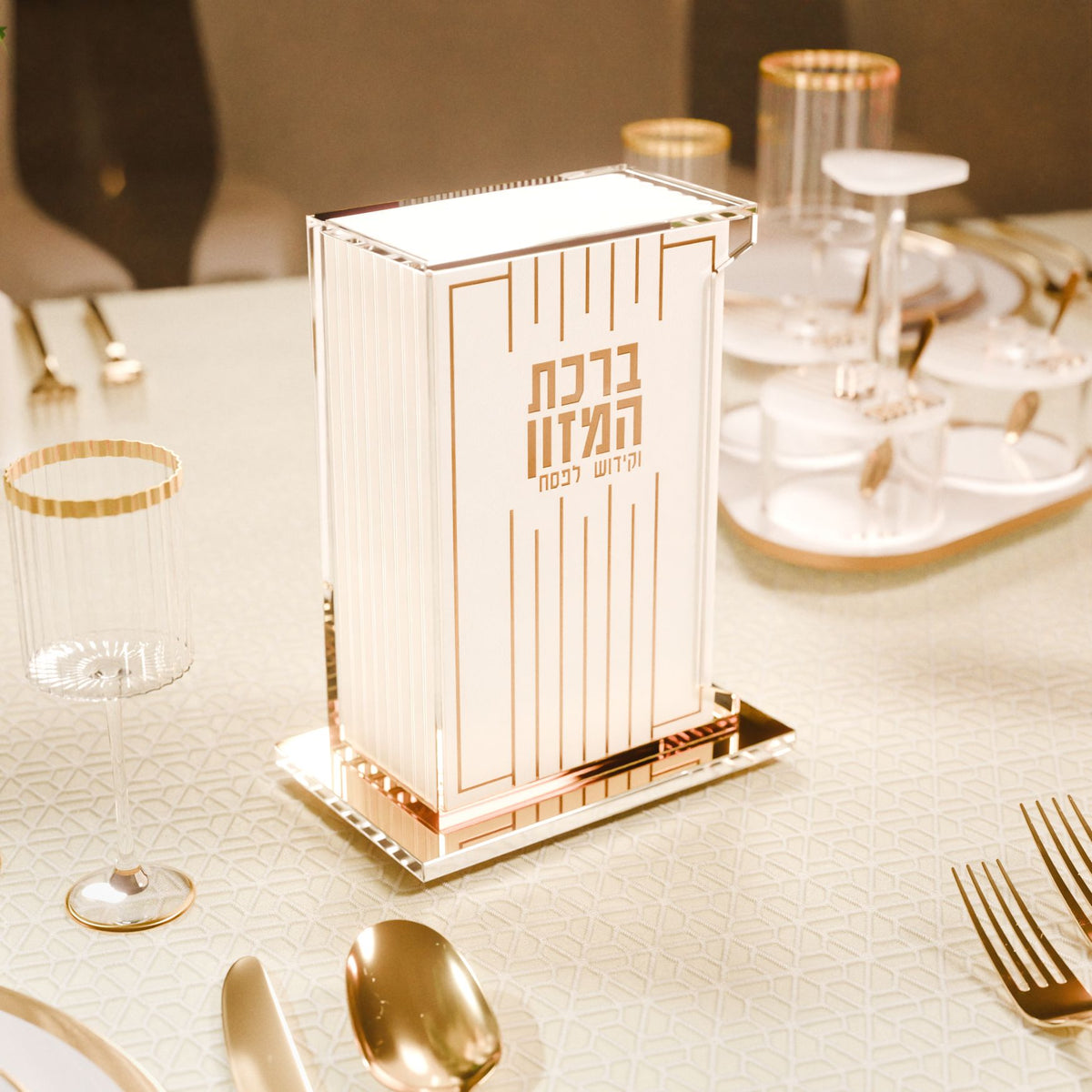 Gold Pesach bencher set on a Seder table with gold cutlery and glassware