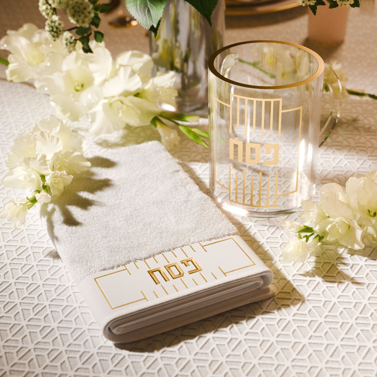 Gold Pesach washing cup on a table beside a folded towel and white flowers