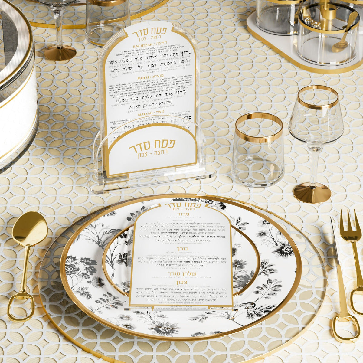 Gold Seder card set above a floral plate at a set Pesach table with gold-rim glasses