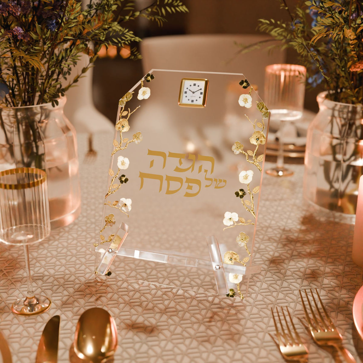 Haggadah stand on a Seder table set with gold cutlery, glassware and flowers in warm light