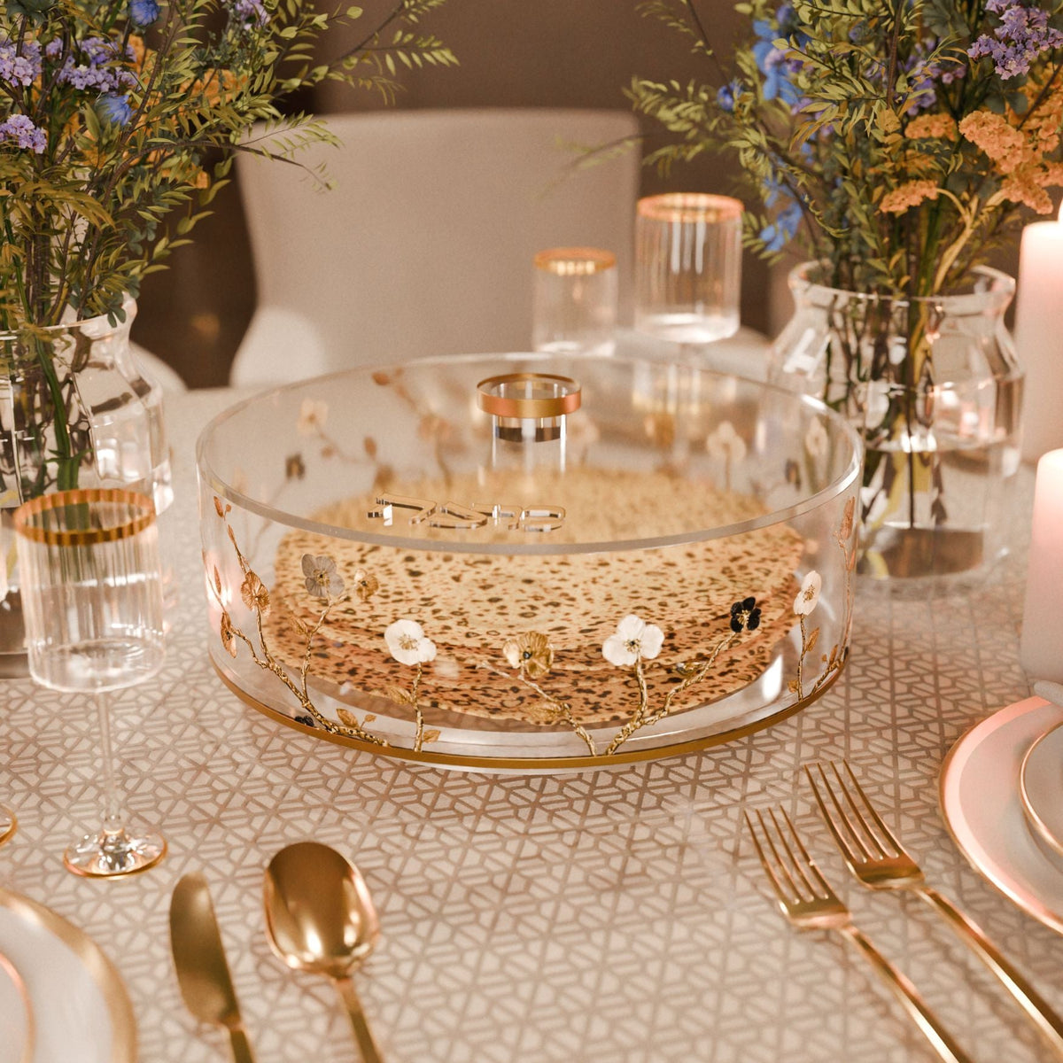 Matzah box filled with round matzos on a Seder table with gold cutlery, glassware and flowers
