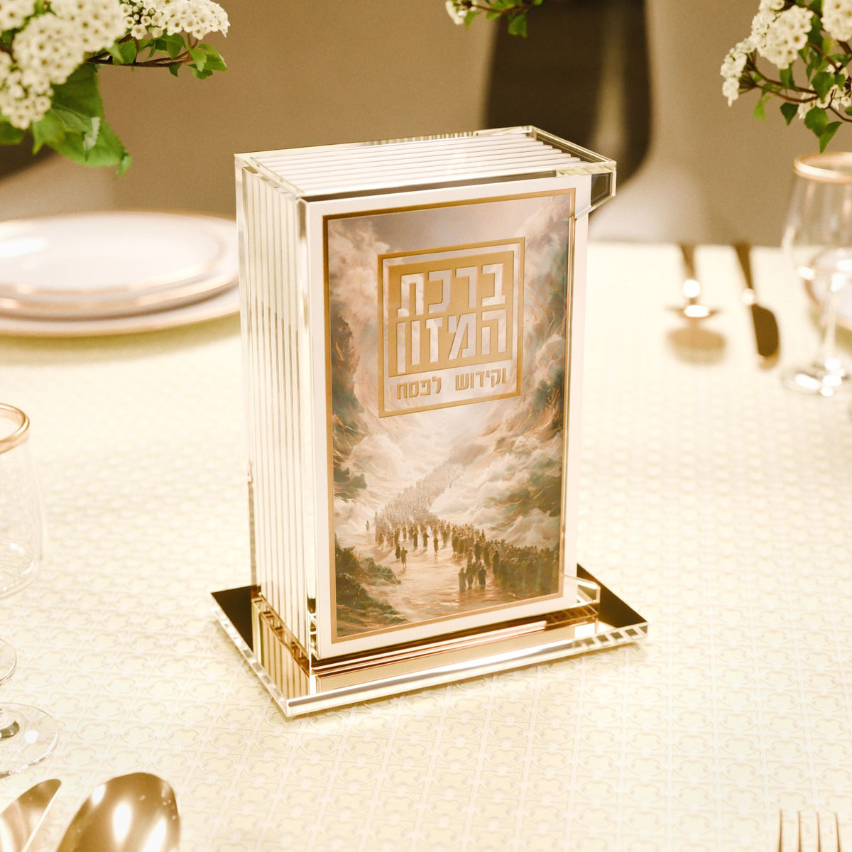Pesach bencher set standing on a white Yom Tov table with flowers and place settings