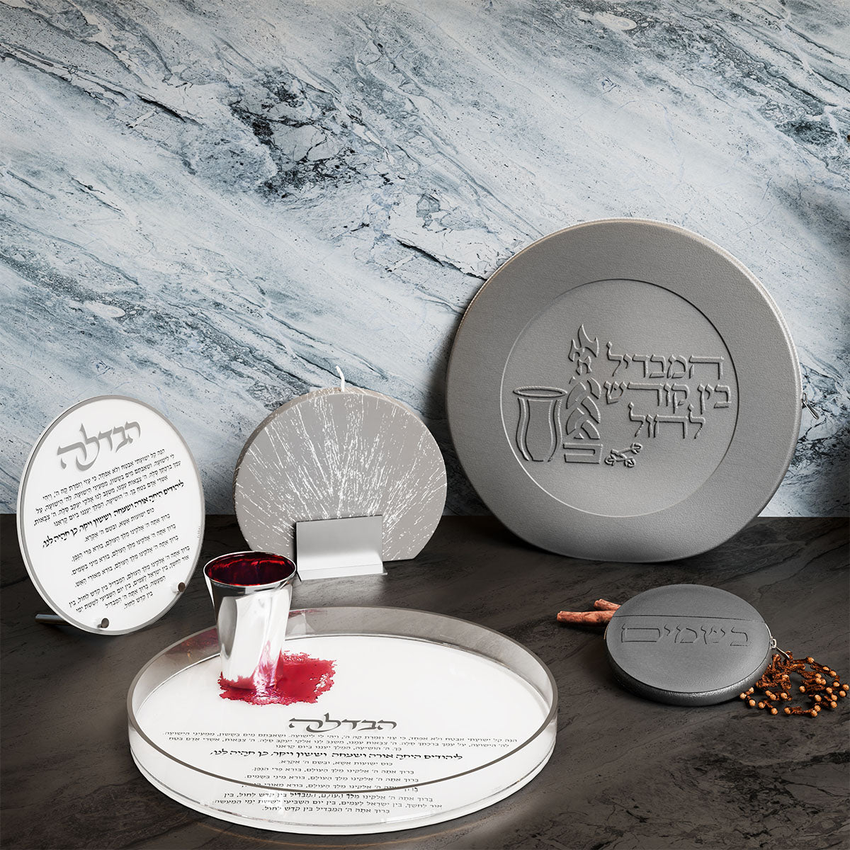 Silver Havdalah tray with a cup of wine beside a round Havdalah card, plaque and spice tin on slate