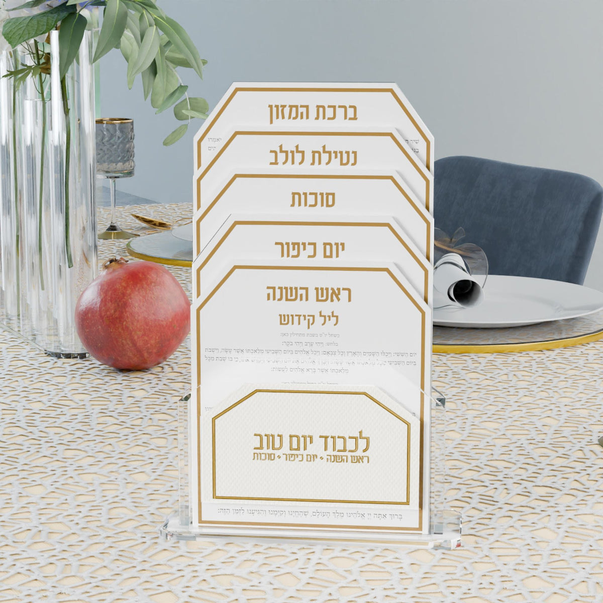 Gold Tishrei cards on a Yom Tov table next to a pomegranate and a place setting