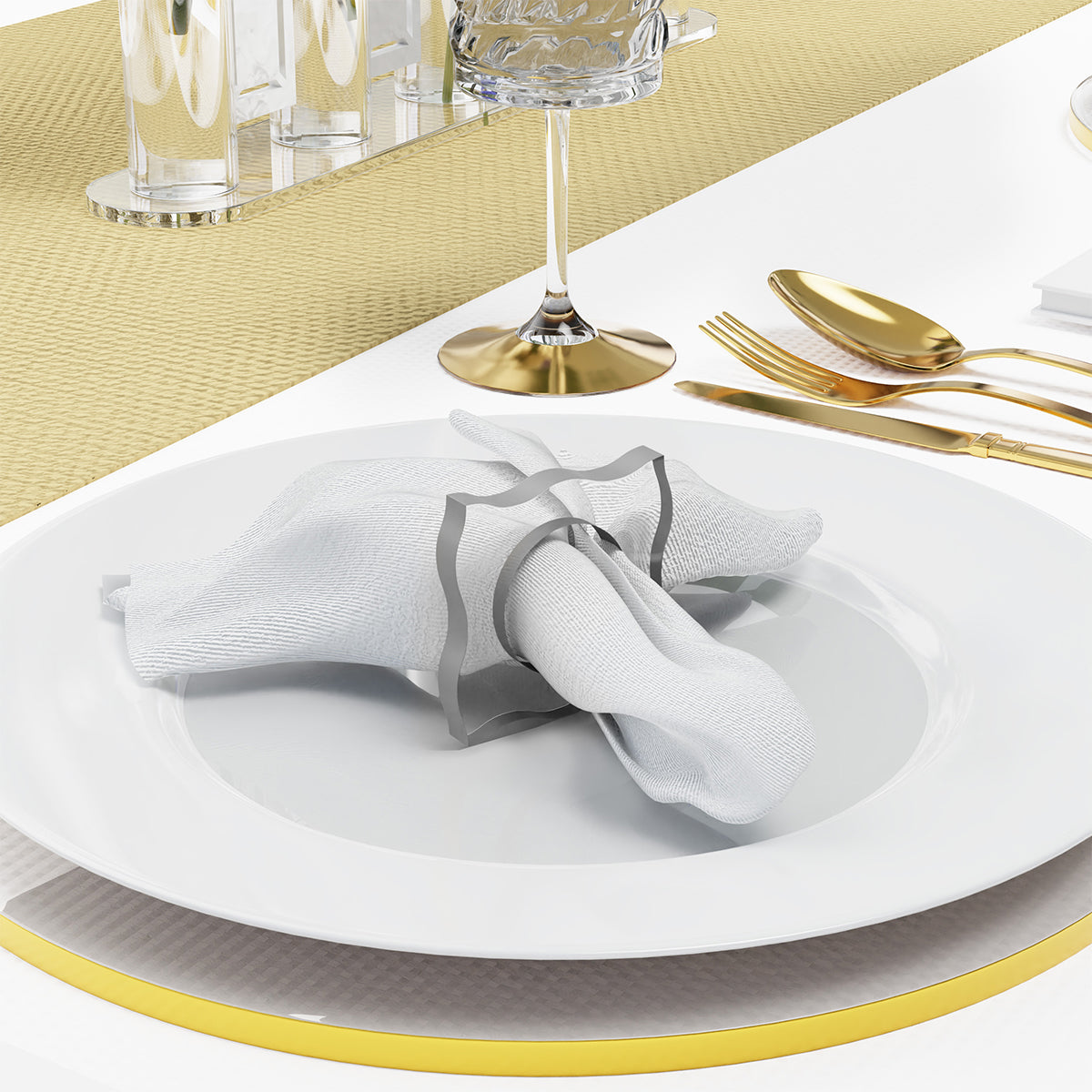 Silver napkin ring and napkin on a white plate beside gold flatware and stemware