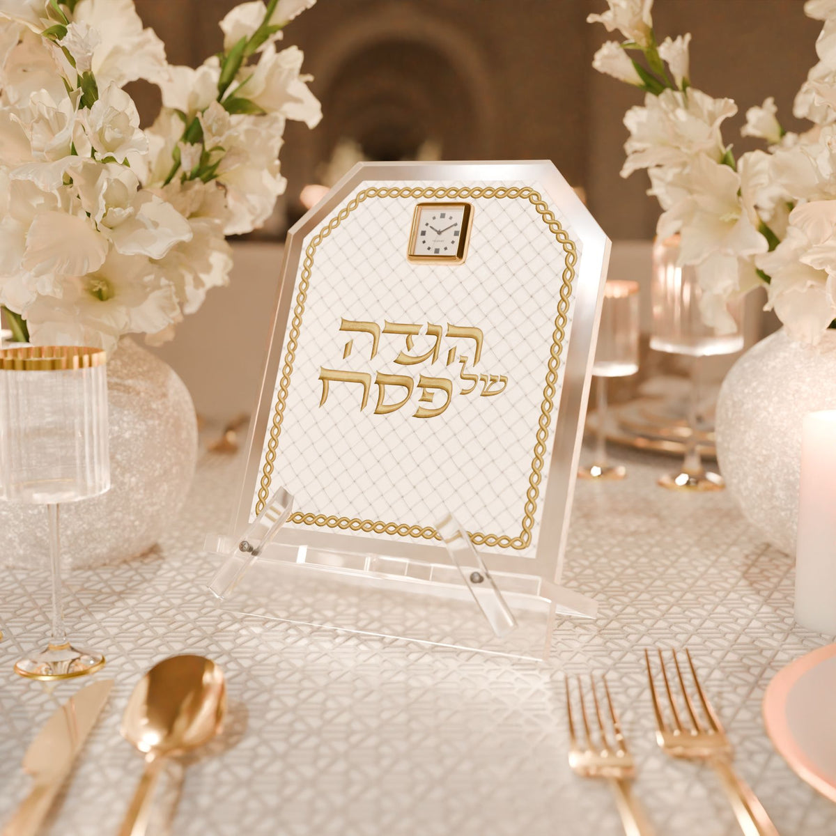 Gold Haggadah stand on a seder table set with gold flatware, white flowers and candles