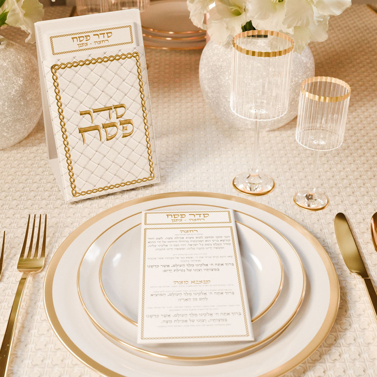 Card pouch at a Seder place setting with gold-rimmed plates and glasses, a card resting on the plate