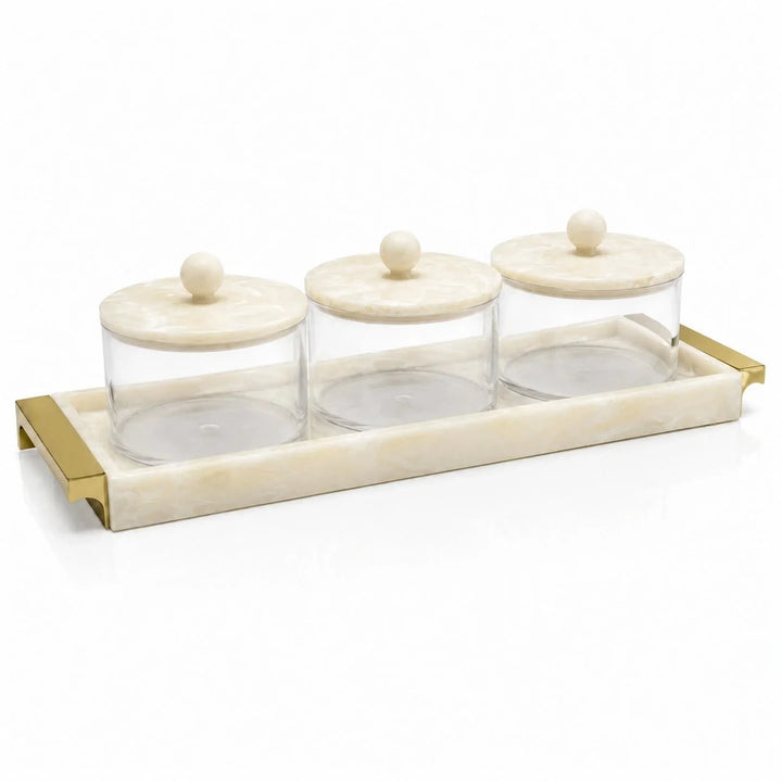 Three lidded glass bowls in a marbleized tray with gold handles, on a white background