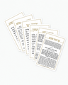 White credit-card-size tefillah cards fanned out, each with a thin gold frame and gold Hebrew heading, the Krias Shema card in front and the Birchas Hamazon card behind it