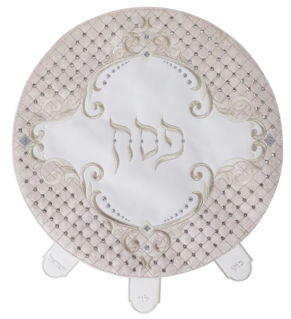 Round matzah cover with a blush quilted faux-leather border set with crystals, white velvet center embroidered Pesach in silver scrollwork and three labeled pocket tabs at the lower edge