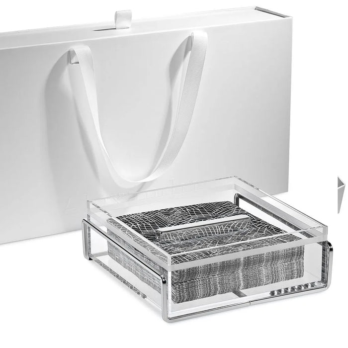 Square clear acrylic napkin holder with silver frame and weight bar on grey napkins, white box behind