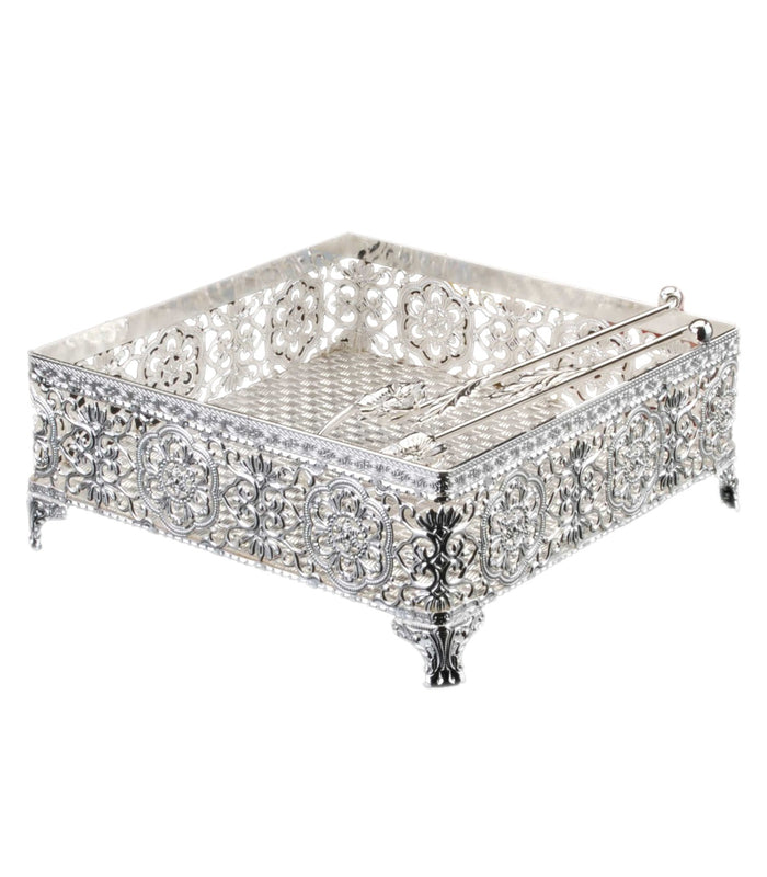 Square silver-plated filigree napkin holder on four scrolled feet with weighted arm across the top
