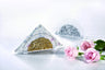 Clear half-round acrylic napkin holder with gold flake filling its lower half, holding a stack of floral napkins, a silver-flake version standing behind it and pink roses alongside