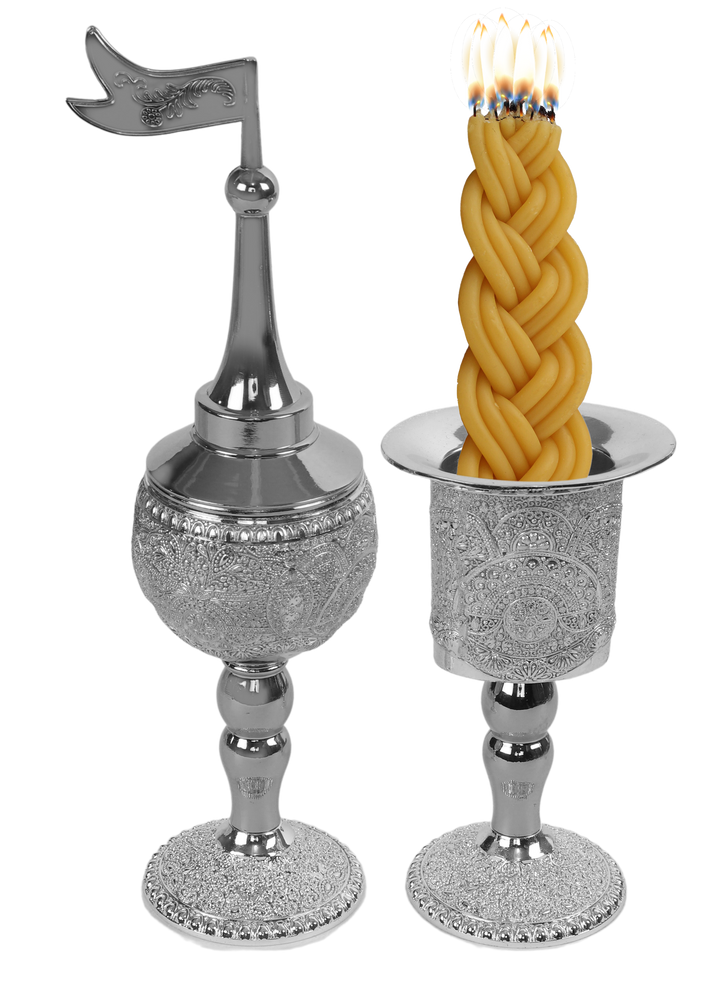 Silver-plated filigree besamim holder with a pointed dome and flag finial beside a matching filigree candle holder with a lit braided havdalah candle in it