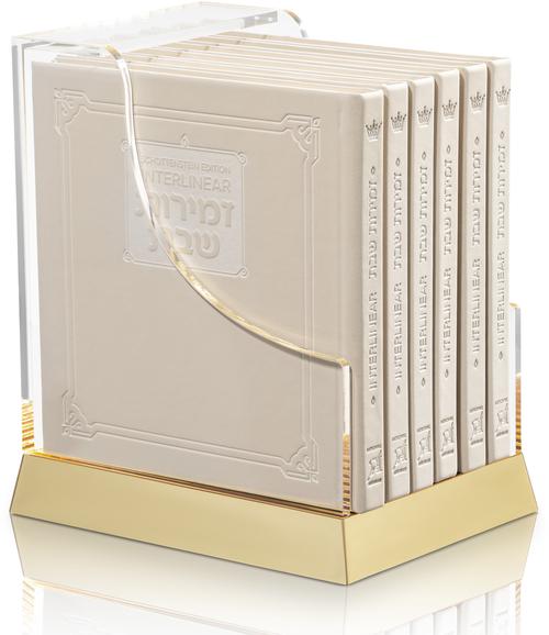 Six cream faux-leather interlinear zemiros volumes in a lucite case, each book 6 by 6 inches.
