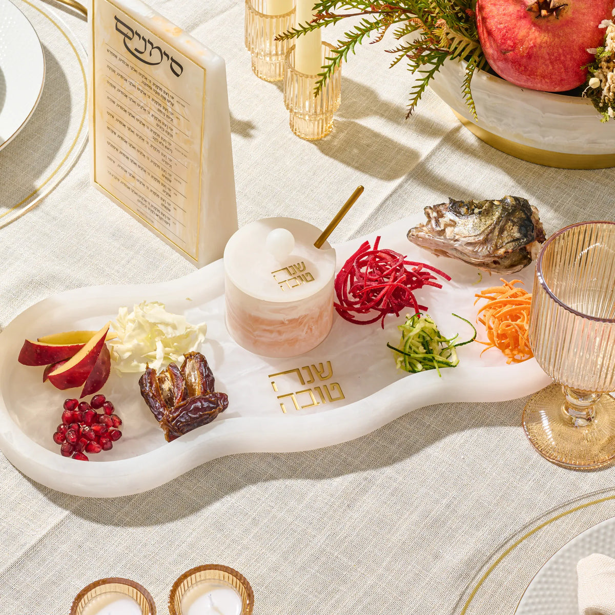 Curved resin Simanim tray on a table set with apple, pomegranate, dates, carrot and beet strands