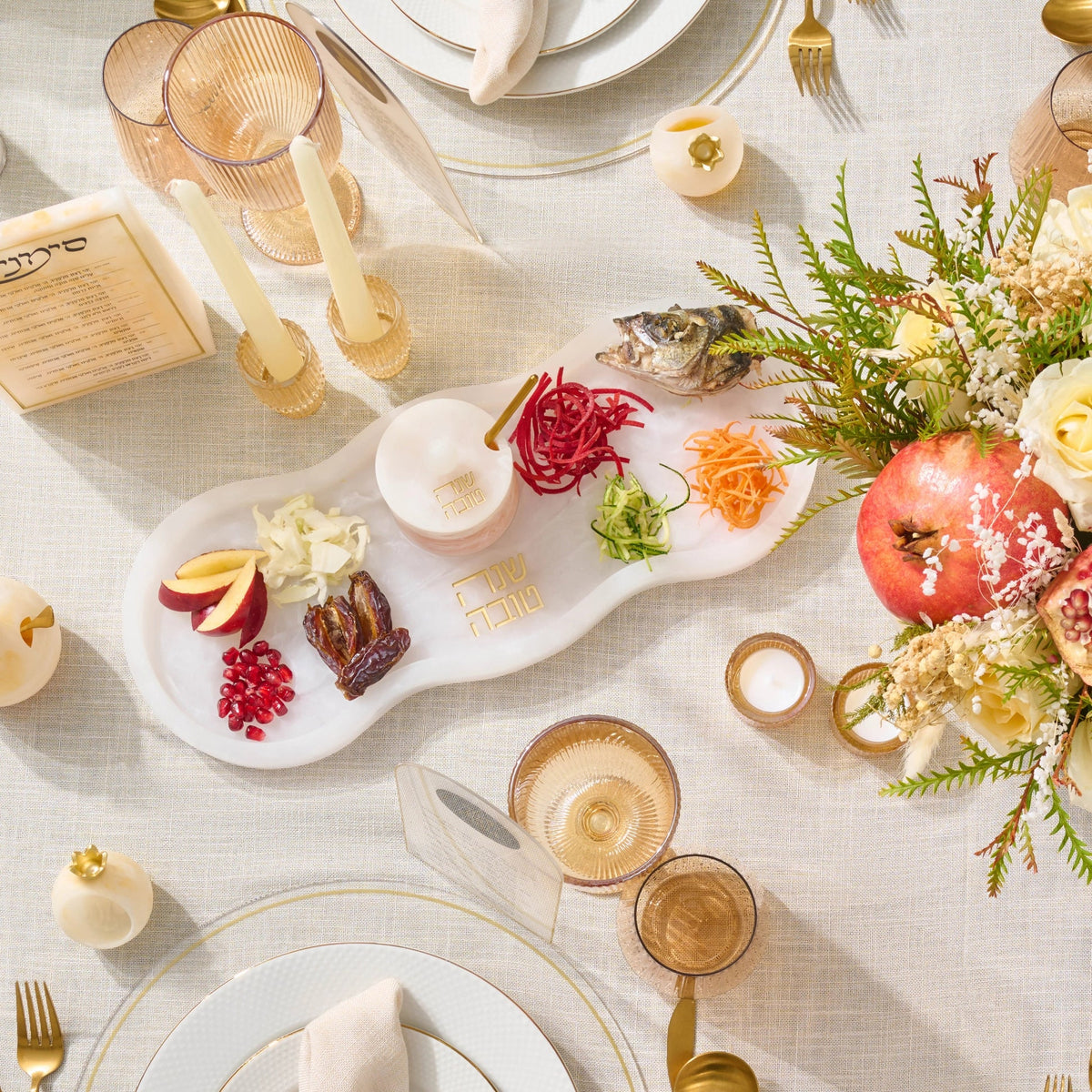 Overhead view of the curved Simanim tray set among gold flatware, pomegranate centerpiece, and fish