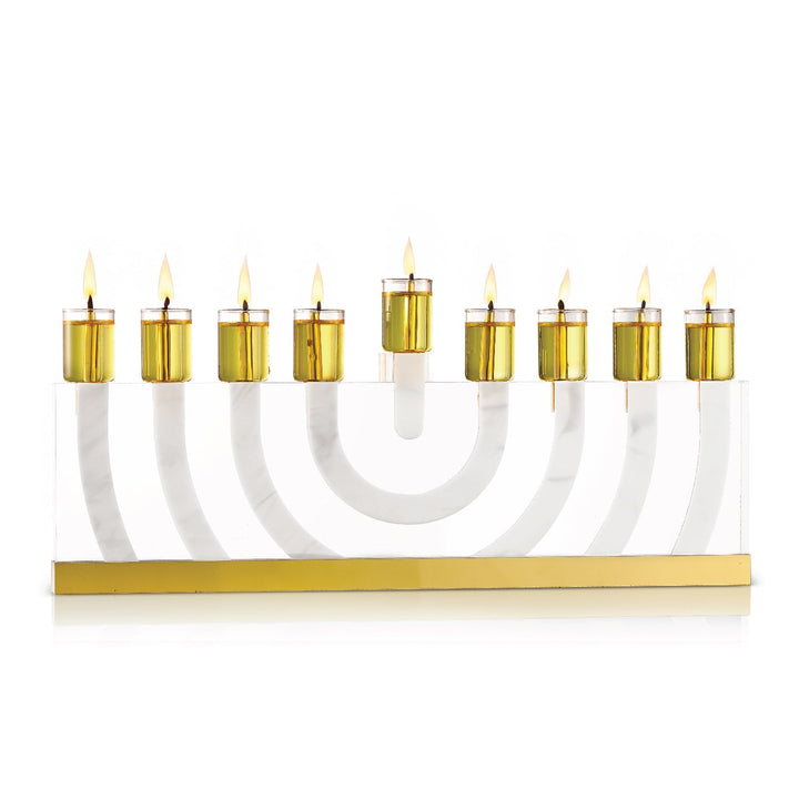 Clear lucite arc menorah with gold cups lit, standing on its gold mirror base