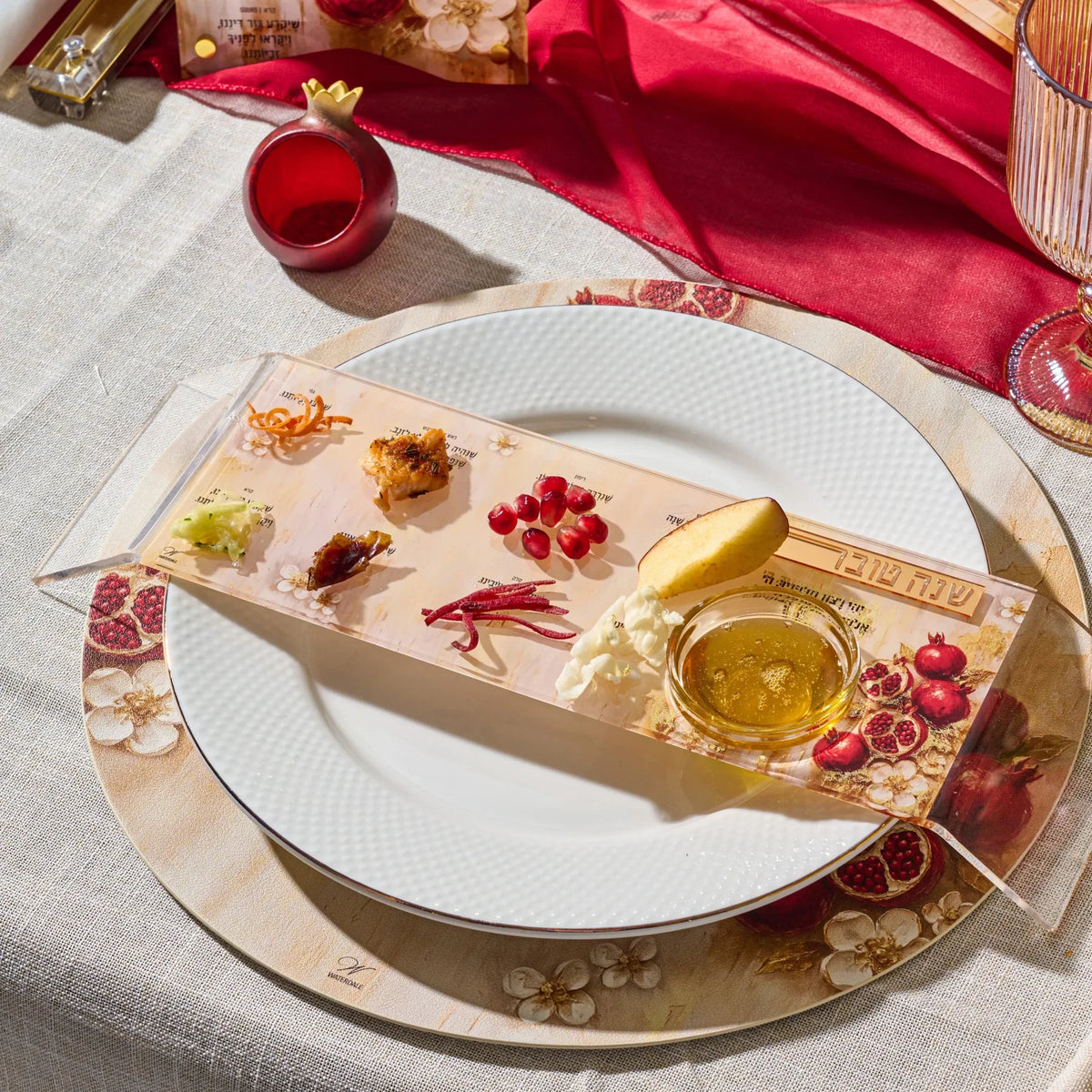 Painted pomegranate Lucite simanim tray arranged with symbolic foods at a place setting