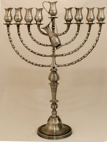 Tall pewter oil menorah with tulip cups on curved segmented arms and a sculpted pitcher at the center