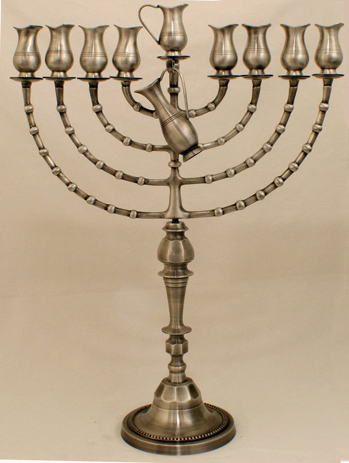 Tall pewter oil menorah with tulip cups on curved segmented arms and a sculpted pitcher at the center