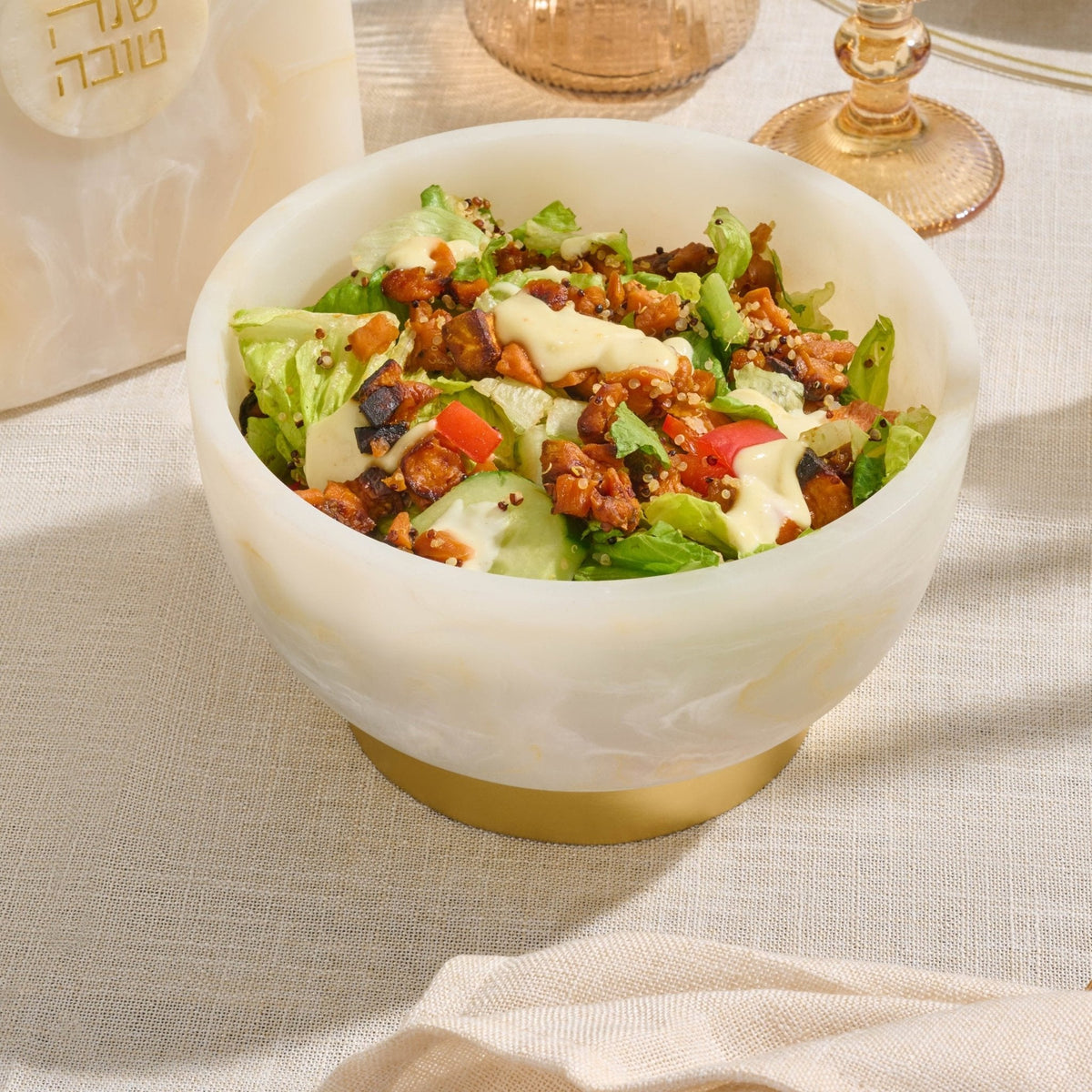 Marbled resin pedestal bowl filled with salad on a table set with wine glasses