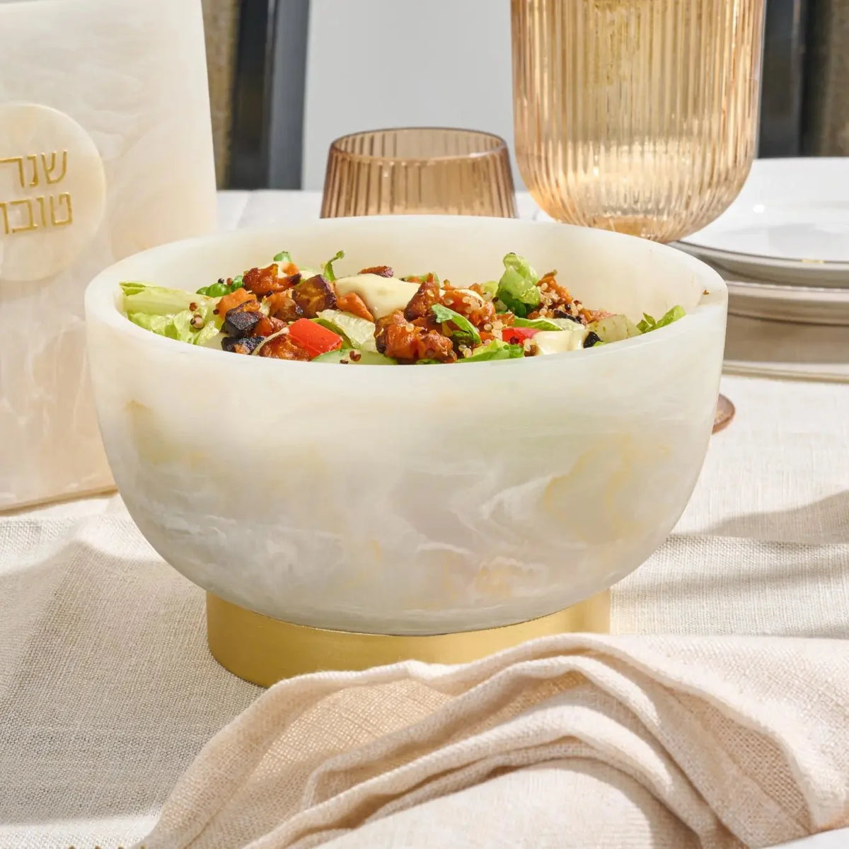 Marbled resin pedestal bowl of salad on a table set with amber-tinted glassware