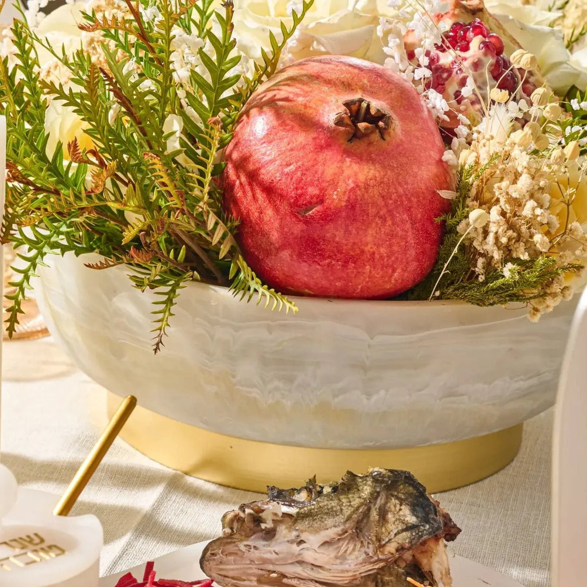 Marbled resin pedestal bowl filled with a pomegranate and floral centerpiece arrangement