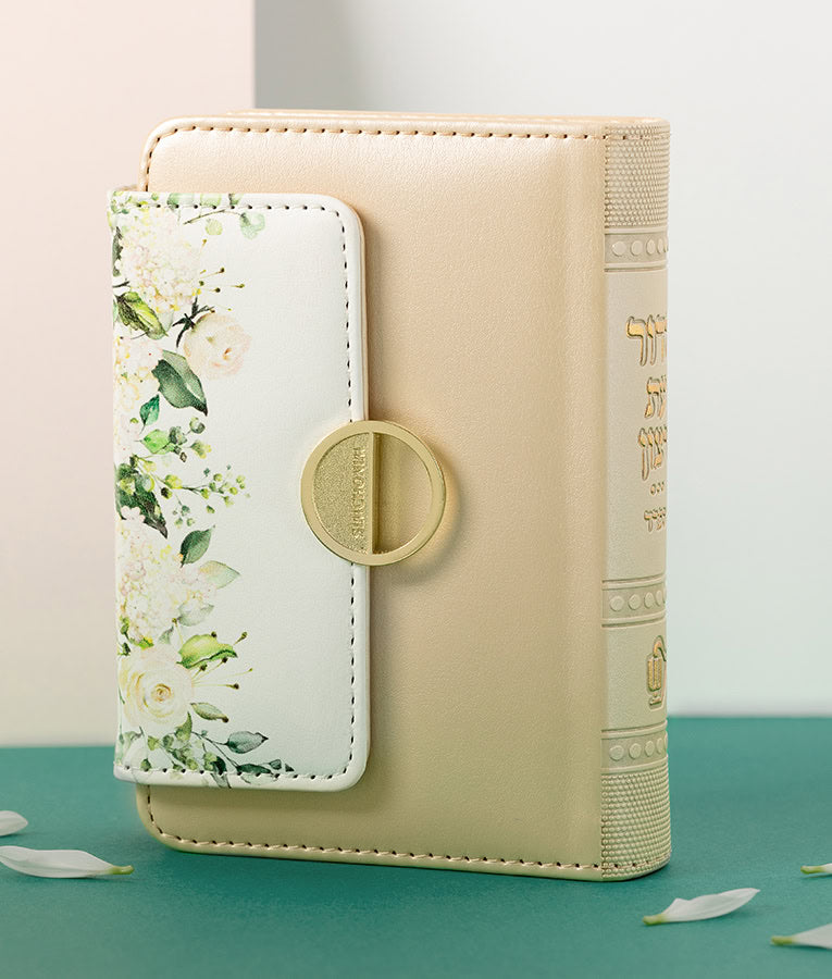 Simchonim Floral style pocket siddur in cream, shown on a table setting