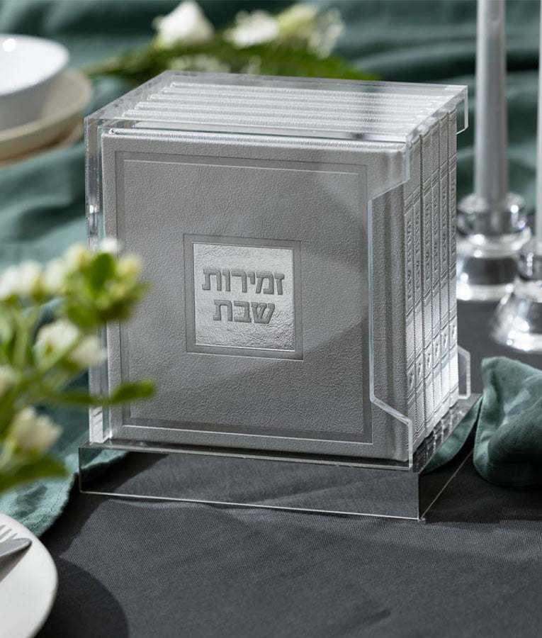 Simchonim Lucite stand holding hardcover zemiros in silver, shown on a table setting