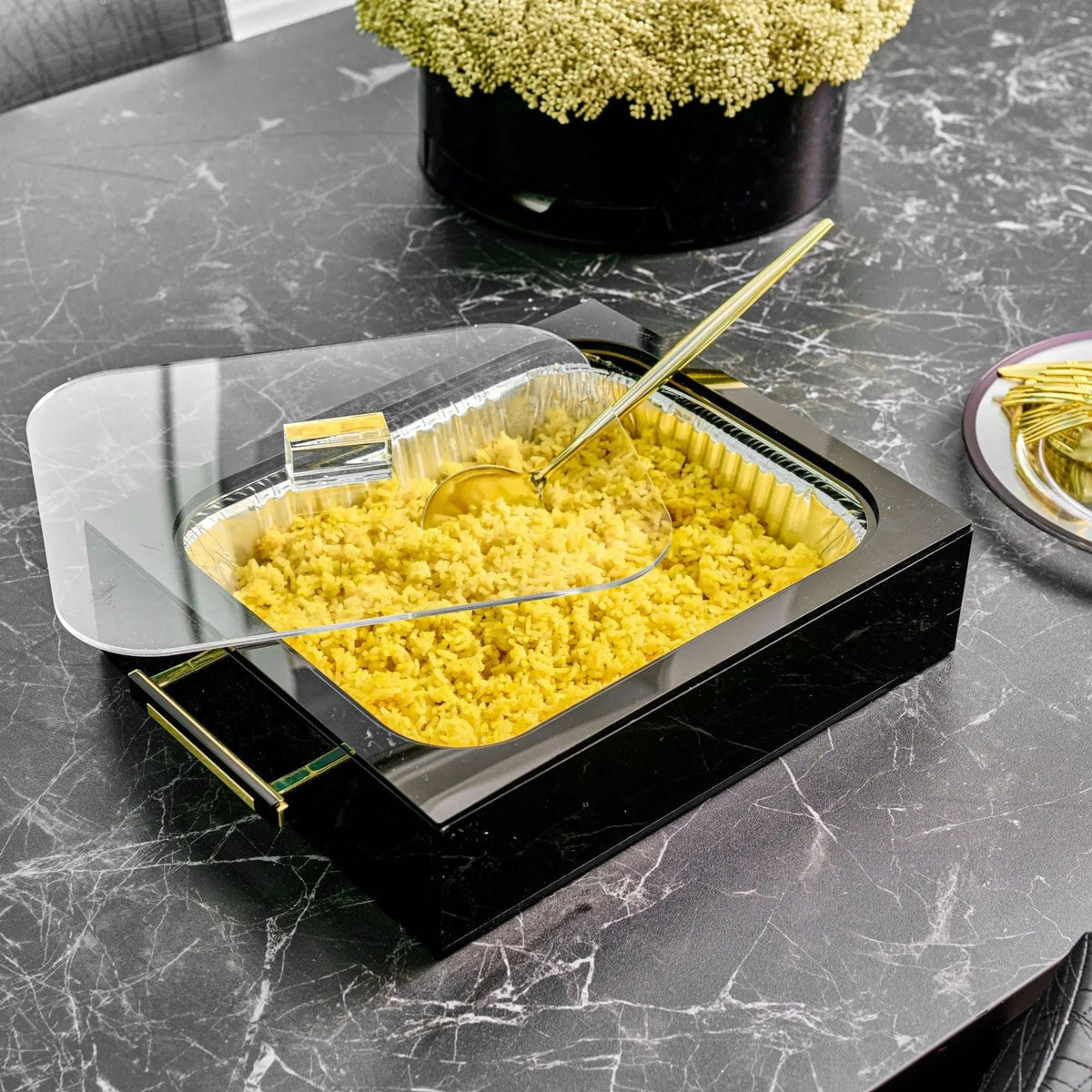 Black lucite pan holder in use on a marble table with a filled foil pan and the lid resting behind it