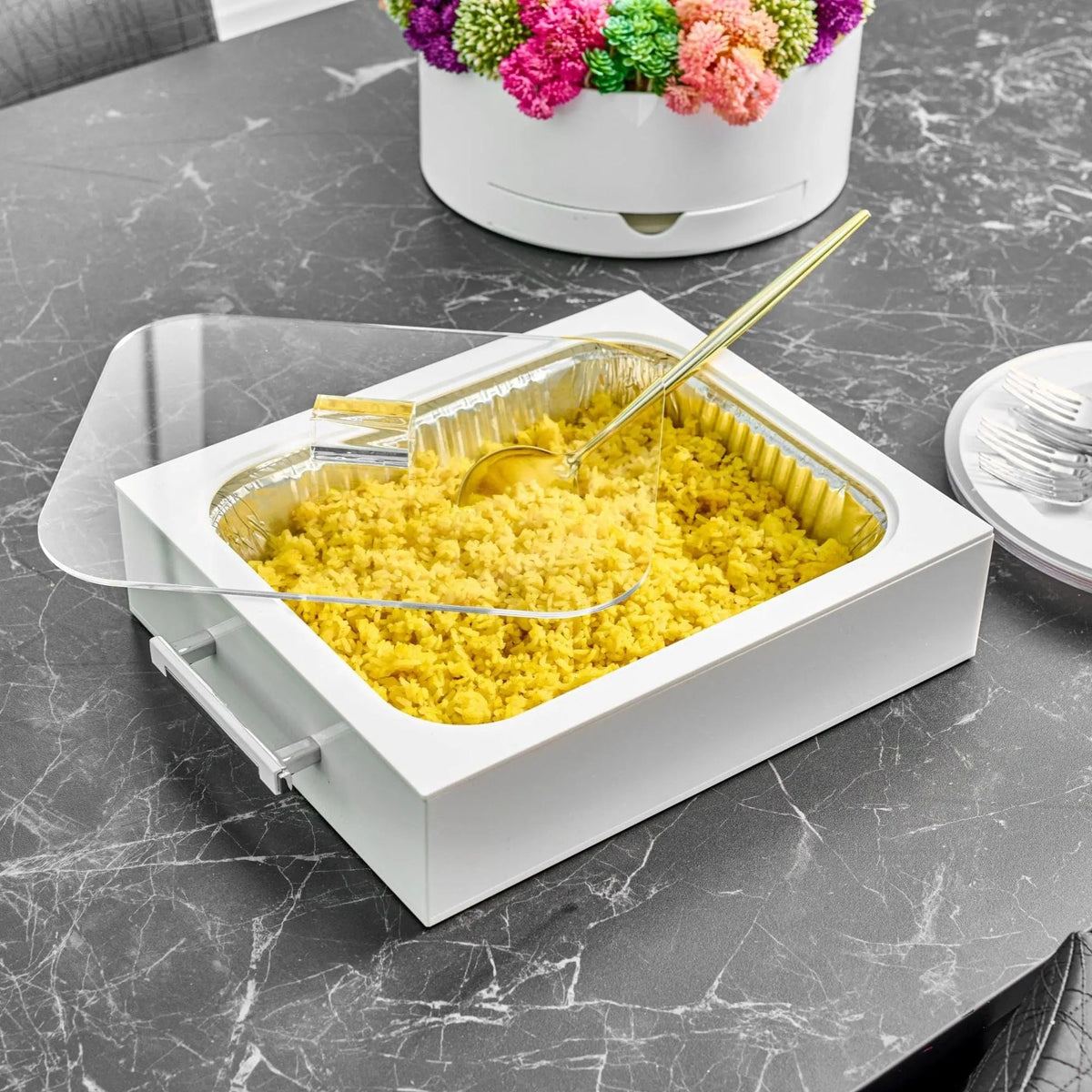 White lucite pan holder on a marble table, foil pan filled with rice, gold serving spoon, lid set aside