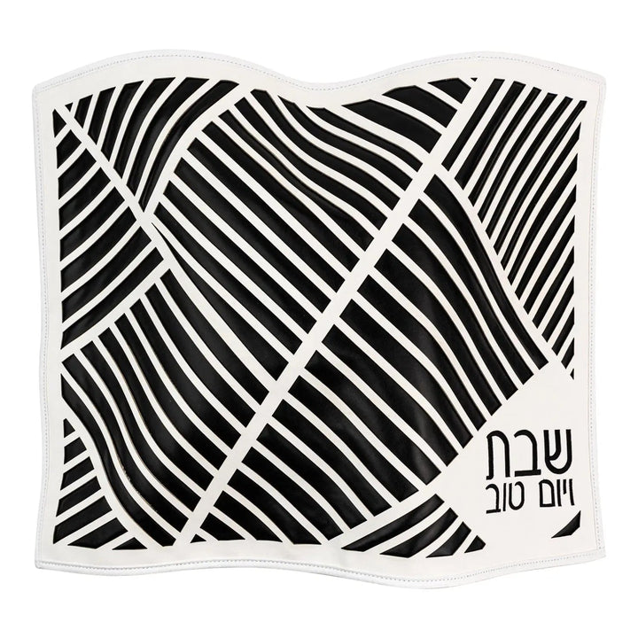 Black and white diagonal laser-cut leather challah cover with embossed 'שבת ויום טוב' text, flat top view